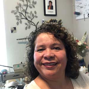 carmen in her taylor shop with a sewing machine and spools of thread